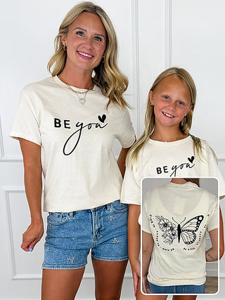 Cream short-sleeve graphic tee with black "Be You" text design