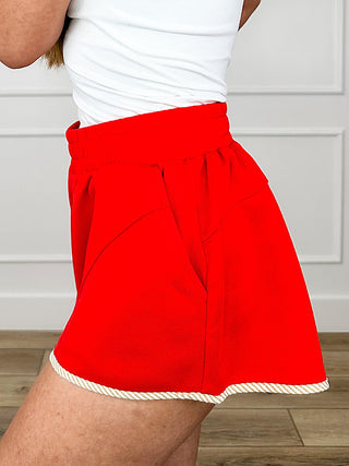 Red high-rise knit shorts, tied waist look, front patch pockets, ruffled hem