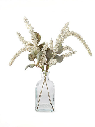 Cream floral decor stems with bead-like branches and green leaves in clear glass vase