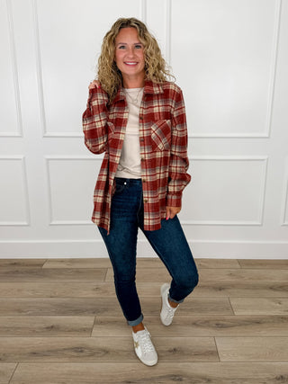 Brick red and cream plaid flannel shacket worn over a cream top with dark wash skinny jeans and white star sneakers.