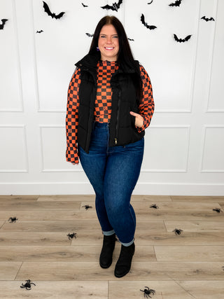 Model wears an orange and black checkered pumpkin print sheer mesh top with a black puffer vest and Judy Blue Kyla jeans.