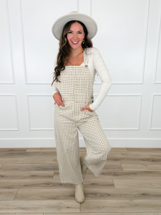 Cream and tan gingham check overalls layered over a white top with a cream panama hat and booties.