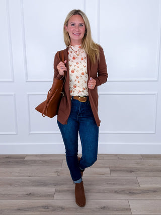 Brown cardigan over floral mesh top with dark jeans and belt, paired with brown boots