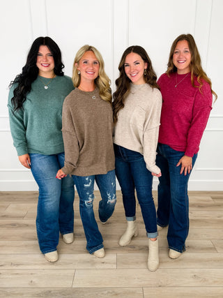 Four women wearing green, taupe, oatmeal, and wine brushed knit tops styled with jeans and booties.