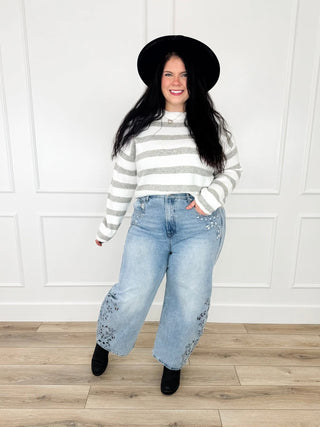 Grey and white striped knit sweater worn with light wash embroidered wide leg jeans, black booties and a black hat.