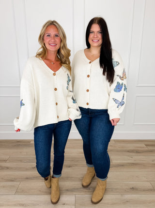 Ivory knit cardigan with blue butterfly appliques on the sleeves worn with dark wash skinny jeans and tan booties.