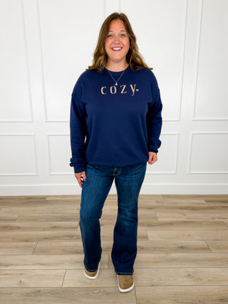 Navy Cozy graphic crewneck sweatshirt styled with dark wash bootcut jeans and tan suede clogs.