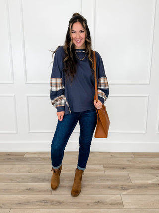 Navy waffle knit top with rust and cream plaid sleeve panels worn with dark wash skinny jeans and brown booties.