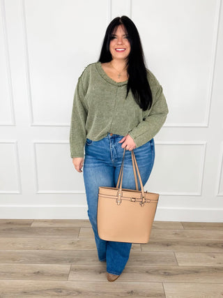 Olive waffle knit V neck top with exposed seams worn with light wash flare jeans and a tan tote.