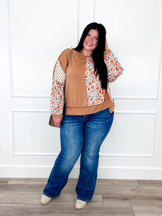 Tan mixed print top with floral and striped sleeves styled with dark wash straight leg jeans.