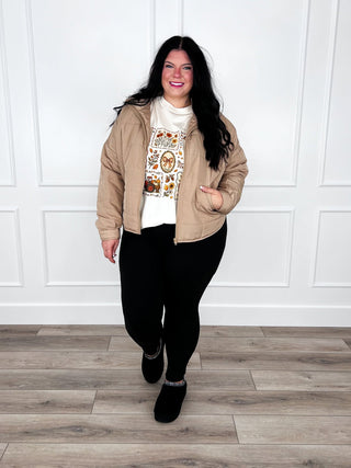 Tan lightweight puffer jacket over a cream fall graphic tee with black leggings.