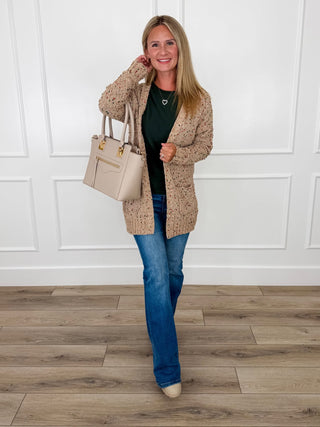Tan popcorn knit cardigan flecked with rust and green worn over a forest green sweater with light wash flare jeans.