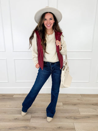 Wine quilted hooded vest layered over a cream knit sweater with dark wash bootcut jeans and cream booties.