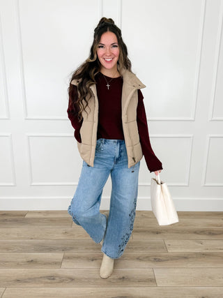 Wine textured knit sweater with raw edge trim layered under a tan puffer vest with light wash embroidered wide leg jeans.