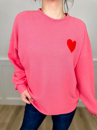 Pink knit long-sleeve top with red heart graphic near the right chest