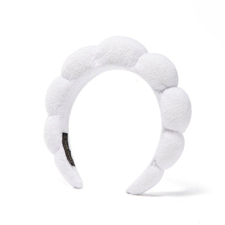 White plush bubble headband with scalloped pads and black logo patch.