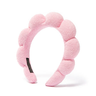 Pink plush bubble headband with scalloped pads and black logo patch.