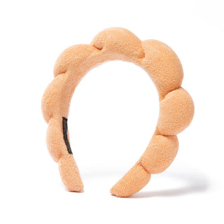 Peach plush bubble headband with scalloped pads and black logo patch.