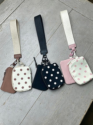 Three wristlet pouches with polka-dot fronts and wrist straps, in brown, black, and pink