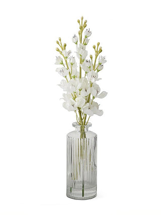 Ivory faux delphinium decor in clear glass vase with white flower stems and green buds
