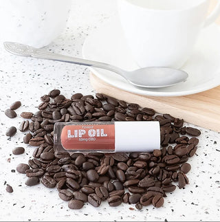 Tinted CBD lip oil in a brown shade bottle beside coffee beans, 50mg CBD.
