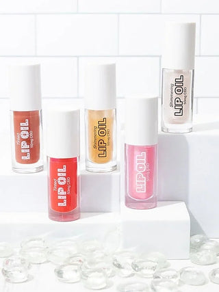 Set of tinted CBD lip oil bottles in red, gold, and pink shades with white caps.