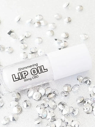 Shimmering CBD lip oil bottle with label text, surrounded by silver glitter pieces.
