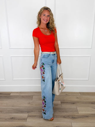Red short sleeve top with light wash floral embroidered wide leg jeans and a belt.