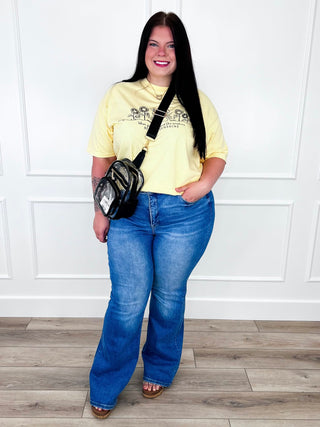 Yellow "Be the Sunshine" sunflower graphic tee with medium wash flare jeans and a clear belt bag.