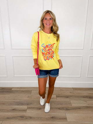 Yellow graphic crewneck sweatshirt with colorful sunset text paired with cuffed denim shorts and white sneakers.