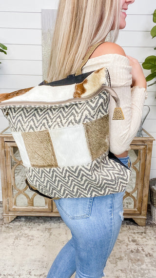 Colorblock cowboy backpack shown from side, patterned front, tan flap patch, dangling tassel.